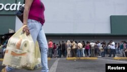 FILE - A woman carries bags with toilet paper rolls as people line up to buy staple items at a Makro supermarket in Caracas Aug. 4, 2015.