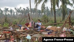 This photo taken on Dec. 18, 2021 and received on Dec. 19 from the Philippine Coast Guard shows a resident drying her clothes on the ruins of a home in Del Carmen town in Surigao del Norte province. (Photo by Handout / Philippine Coast Guard (PCG) / AFP) 