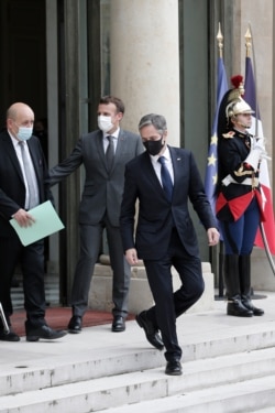 U.S. Secretary of State Antony Blinken leaves as French President Emmanuel Macron, center, gestures toward French Foreign Minister Jean-Yves le Drian, left, at the Elysee palace, June 25, 2021.