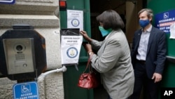 A voter, left, places a ballot in a secure box as Providence City Clerk Shawn Selleck, right, looks on, Tuesday, June 2, 2020, in Providence, R.I. Because so many voters asked for mail ballots, state electoral officials say mail ballots can be dropped off