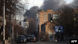 Mobil melaju di jalan sementara asap mengepul dari api setelah serangan roket di pusat kota Kyiv pada 29 Desember 2023, di tengah invasi Rusia ke Ukraina. (Foto: AFP)