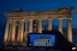 A woman holds up a mobile phone showing a digitally overlayed virtual reconstruction of the ancient Parthenon temple, at the Acropolis Hill in Athens, Greece on Tuesday, June 13, 2023. (AP Photo/Petros Giannakouris)
