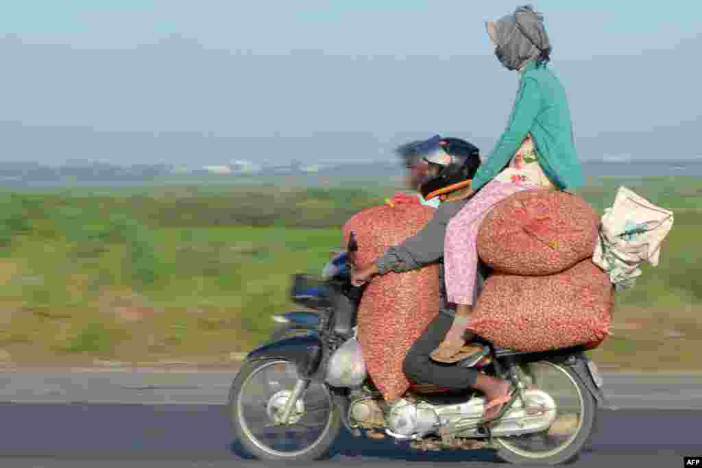 A motorcyclist ferries a pillion rider sitting on goods in Phnom Penh, Cambodia.