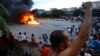 A Buddhist monk shouts as people gather to watch a burning military police car near a polling station in Phnom Penh, Sunday, July 28, 2013. 
