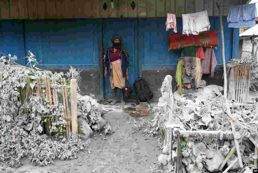 Seorang wanita berdiri di luar rumahnya menyaksikan halaman rumahnya yang tertutup oleh abu vulkanik dari letusan Gunung Sinabung, di Mardinding, Sumatera Utara. 