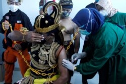 Seorang petugas kesehatan menyuntikkan vaksin Sinovac ke seorang pria yang mengenakan kostum wayang manusia tradisional Indonesia yang dikenal sebagai Wayang, di Jawa Tengah. (Foto: Antara via Reuters)
