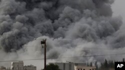 Asap tebal terlihat setelah serangan udara yang dipimpin AS di Kobani, Suriah, seperti terlihat dari pinggiran Suruc, di perbatasan Suriah dan Turki, Minggu (12/10).