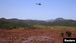 FILE - A helicopter flies over the Bento Rodrigues district, covered with mud after a dam owned by Vale SA and BHP Billiton Ltd. burst in Mariana, Brazil, Nov. 6, 2015. 