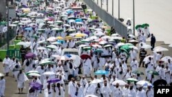 Para jemaah haji membawa payung untuk melindungi dari terik matahari, tiba di pemondokan jemaah, tenda Mina, di tengah pelaksanaan ibadah Haji di dekat Makkah, Jumat, 14 Juni 2024. (Foto: Fadel Senna/AFP)