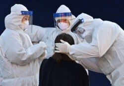 A medical staff member wearing protective gear takes a swab from a woman to test for the COVID-19 coronavirus at a temporary testing station outside Seoul station in Seoul, Dec. 14, 2020.