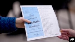 A woman takes a Democratic ballot to vote in the New Hampshire Primary at Parker-Varney Elementary School, Tuesday, Feb. 11, 2020, in Manchester, N.H. (AP Photo/Andrew Harnik)