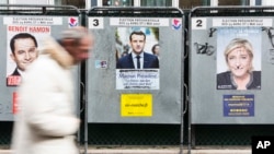 A man walks past campaign posters featuring French presidential candidates Benoit Hamon, left, Emmanuel Macron, center, and Marine Le Pen in Paris, France, April 17, 2017. 