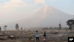 Villagers stand on an area covered in volcanic ash as Mount Semeru looms in the background in Kajar Kuning village in Lumajang, East Java, Indonesia, Monday, Dec. 5, 2022. 