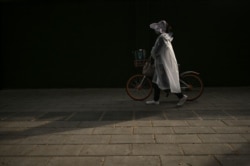 A woman wearing a raincoat and a face mask walks on a street in Wuhan, China's central Hubei province on April 15, 2020.