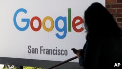 FILE - A person walks past a Google sign in San Francisco, May 1, 2019. 