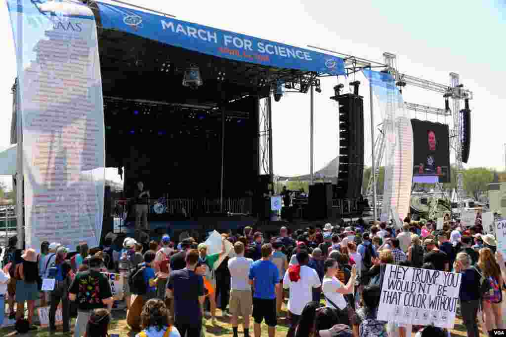 ក្រុម​អ្នក​តវ៉ា​ប្រមូល​ផ្ដុំ​គ្នា​នៅ​ក្បែរ​ឆាក​ដើម្បី​ទស្សនា​ការ​ប្រគុំ​តន្ត្រី​និង​ស្ដាប់​សុន្ទរកថា​ស្ដី​ពី​វិទ្យាសាស្ត្រ។ (ចាប ចិត្រា/VOA)