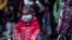 FILE - A young girl wearing a mask to prevent the spread of the coronavirus, looks on after refugees and migrants arrived at the port of Piraeus, near Athens, May 4, 2020. 
