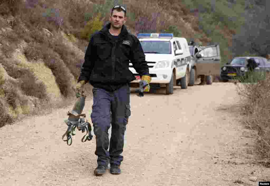 An Israeli police explosive expert carries the remains of a rocket after it landed near the northern town of Kiryat Shmona, Israel, Dec. 29, 2013.&nbsp;