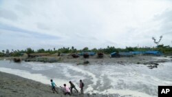Village men walk past as sea water gushes in after breaking an embankment on the Bay of Bengal coast in South 24 parganas, West Bengal state, India, May 25, 2021.