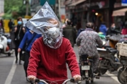A man wearing a face mask and a plastic bag on his head rides a bicycle on a street in Wuhan, China's central Hubei province, on April 14, 2020.