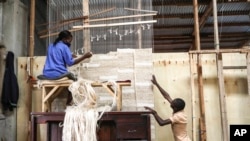 Manager of Texfad, John Baptist Okello, right,speaks to an employee as she weaves a carpet using banana fibre threads, at the TEXFAD factory in Sonde, Mukono District, Uganda, Sept. 20, 2023.