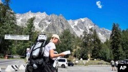 A hiker looks at a map as he walks in a parking lot beneath the Planpincieux glacier, seen at background right, in the Alps on the Grande Jorasses peak of the Mont Blanc massif, in Val Ferret, near Courmayeur, northern Italy, Aug. 7, 2020.