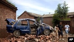 Chinese people walk past a flood-damaged vehicle sitting on the bricks at a village in Fangshan district of Beijing, China, July 23, 2012. 