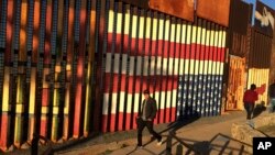 People pass graffiti along the border structure in Tijuana, Mexico, Jan. 25, 2017.