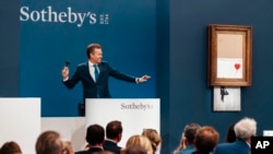 In this handout photo provided by Sotheby's Auction House, the auction for Banksy's "Love is the Bin" takes place in London, Oct. 14, 2021.