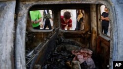 Palestinian kids look at a destroyed car after it was hit in an Israeli airstrike, in Gaza City, May 19, 2021.