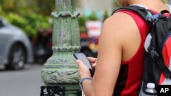 In this Oct. 25, 2017, photo, a man uses his cellphone before crossing a street in Honolulu. A new Honolulu ordinance allows police officers to issue tickets to pedestrians caught looking at a cellphone or electronic device while crossing a city street.