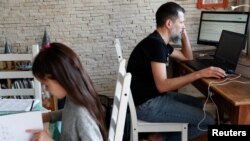 Csaba Posta (kanan), seorang ahli IT, bekerja dari rumahnya bersama dengan anaknya Vilma yang tengah belajar dari rumah mereka di di Budapest, Hungaria, pada 19 Maret 2020. (Foto: Reuters/Bernadett Szabo)