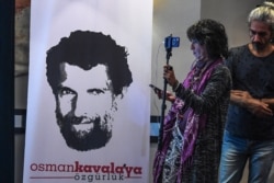 FILE - A journalist stands in front of a poster featuring jailed philanthropist Osman Kavala, during a press conference given by his lawyers, in Istanbul, Turkey, Oct. 31, 2018.