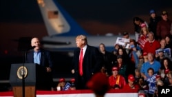 Rep. Greg Gianforte, R-Mont., speaks as President Donald Trump, center, listens during a campaign rally at Minuteman Aviation Hangar, Oct. 18, 2018, in Missoula.