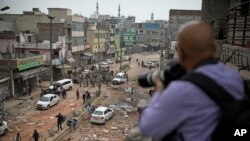 A photojournalist takes photographs of Indian paramilitary soldiers patrolling a street vandalized in Tuesday's violence in New Delhi, India, Feb. 27, 2020.
