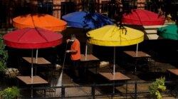 FILE - A worker wearing a mask to protect against the coronavirus power-washes an exterior dining area along the River Walk, in San Antonio, Texas, Aug. 12, 2020.