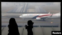 FILE - A woman and a girl look at a Malaysia Airlines plane on the tarmac of Kuala Lumpur International Airport.