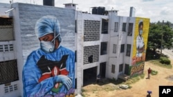 Residents in Mombassa, Kenya, walk in front of informational murals painted on the side of an apartment block about the coronavirus and paying tribute to medical workers with the messages "We'll Protect You" and "We Salute You," Aug. 17, 2020.