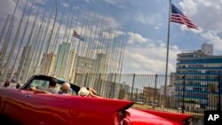 Tourists ride a vintage American convertible as they drive next to the American flag and a Cuban flag at the United States embassy in Havana, Cuba, March 18, 2016.