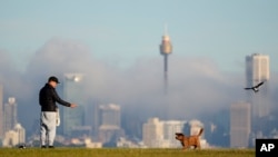 FILE - A man gestures to his dog as fog drifts through the buildings in Sydney's central business district, Australia, June 11, 2021.