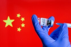 A woman holds a small bottle labeled with a "Coronavirus COVID-19 Vaccine" sticker and a medical syringe in front of displayed China flag, Oct. 30, 2020.