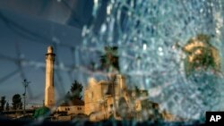 The minaret of the Al-Omari mosque and St. George Greek Orthodox church are reflected in the broken windshield of a vehicle sitting outside a synagogue in the mixed Arab-Jewish town of Lod, central Israel, Wednesday, May 26, 2021.(AP Photo/David Goldman)