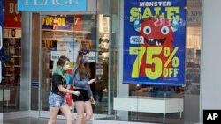 Two girls walk past a store with sale signs displayed at Great Lakes Mall, June 10, 2020, in Mentor, Ohio. The Federal Reserve says the coronavirus pandemic caused a sharp fall in economic activity and a surge in job losses.