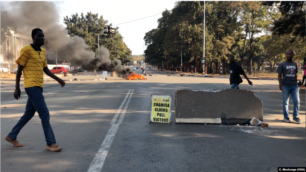 Residents of Harare walk past burning tires, Aug. 1, 2018, after protesters blocked some roads in hopes of forcing the release of the results of the July 30 elections.