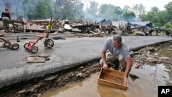 Mark Lester membersihkan kotak dengan air sungai kecil menyusul banjir parah di White Sulphur Springs, West Virginia (24/6). (AP/Steve Helber)