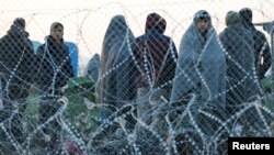 Migrants stand behind a border fence at the Greek-Macedonian border, after additional passage restrictions imposed by Macedonian authorities left hundreds of them stranded near the village of Idomeni, Greece, Feb. 23, 2016.