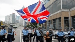 ស្រ្តី​ម្នាក់​គ្រវី​ទង់ជាតិ​អង់គ្លេស​ខណៈដែល​ប៉ូលិស​​ប្រឆាំង​កូប​កម្ម​ឈរ​យាម​បាតុករ​នៅ​ក្បែរ​ទីស្តី​ការ​គណៈរដ្ឋ​មន្រ្តី​កាល​ពី​ថ្ងៃទី​១២ ខែមិថុនា ឆ្នាំ២០១៩។