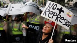 Seorang pendukung oposisi berdiri di hadapan pasukan keamanan anti huru hara dengan memegang sebuah kertas bertuliskan "Tidak ada penindasan lagi" dalam sebuah aksi unjuk rasa melawan Presiden Nicolas Maduro di Caracas, Venezuela, 12 Mei 2017. ( REUTERS/Carlos Garcia Rawlin)