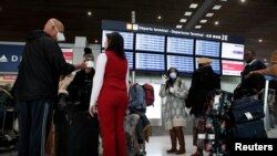 Travellers wearing protective face masks stand at the Delta Air Lines ticketing desk inside Terminal 2E at Paris Charles de Gaulle airport in Roissy, France, March 12, 2020.