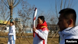 Pembawa obor Li Shucheng melewati nyala api Olimpiade di Taman Olimpiade Musim Dingin, dengan Shougang Udara Besar sebagai latar belakang. (Foto: REUTERS/Norihiko Shirouzu)